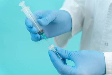 Tıbbi maskeli bir erkek doktor mavi arka planda Corona virüsü aşısı olan bir şırınga tutuyor. Grip, kızamık, koronavirüs aşısı aşısı aşısı. Coronavirus aşısı.