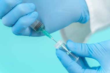 Tıbbi maskeli bir erkek doktor mavi arka planda Corona virüsü aşısı olan bir şırınga tutuyor. Grip, kızamık, koronavirüs aşısı aşısı aşısı. Coronavirus aşısı.