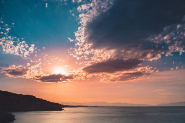 Dağların ve derin mavi okyanusun üzerinde inanılmaz renkli gökyüzü gün doğumu. Gün batımında deniz manzarası.