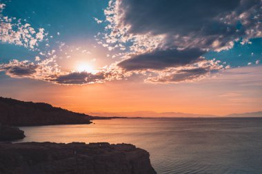 Dağların ve derin mavi okyanusun üzerinde inanılmaz renkli gökyüzü gün doğumu. Gün batımında deniz manzarası.