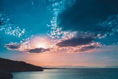 Dağların ve derin mavi okyanusun üzerinde inanılmaz renkli gökyüzü gün doğumu. Gün batımında deniz manzarası.