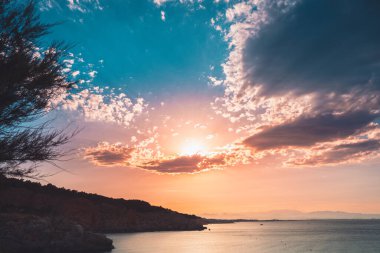 Dağların ve derin mavi okyanusun üzerinde inanılmaz renkli gökyüzü gün doğumu. Gün batımında deniz manzarası.