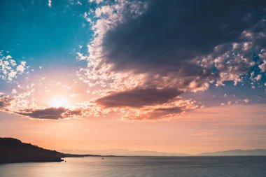 Dağların ve derin mavi okyanusun üzerinde inanılmaz renkli gökyüzü gün doğumu. Gün batımında deniz manzarası.