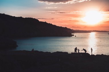 Ailenin silueti, sakin bir okyanusa yansıyan güneşin manzarasına bakıyor. Renkli gökyüzü gün doğumu.