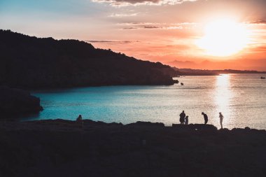 Ailenin silueti, sakin bir okyanusa yansıyan güneşin manzarasına bakıyor. Renkli gökyüzü gün doğumu.