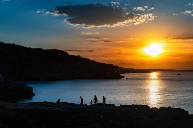 Ailenin silueti, sakin bir okyanusa yansıyan güneşin manzarasına bakıyor. Renkli gökyüzü gün doğumu.