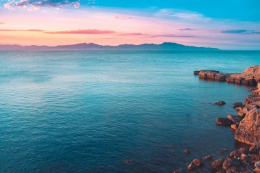 Dağların ve derin mavi okyanusun üzerinde inanılmaz renkli gökyüzü gün doğumu. Gün batımında deniz manzarası.