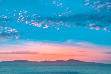 Dağların ve derin mavi okyanusun üzerinde inanılmaz renkli gökyüzü gün doğumu. Gün batımında deniz manzarası.