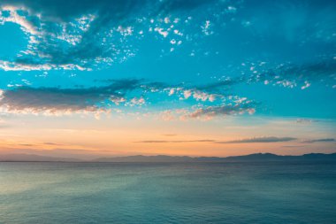 Dağların ve derin mavi okyanusun üzerinde inanılmaz renkli gökyüzü gün doğumu. Gün batımında deniz manzarası.