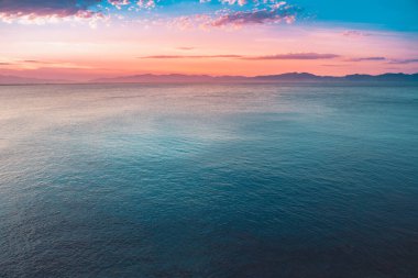 Dağların ve derin mavi okyanusun üzerinde inanılmaz renkli gökyüzü gün doğumu. Gün batımında deniz manzarası.