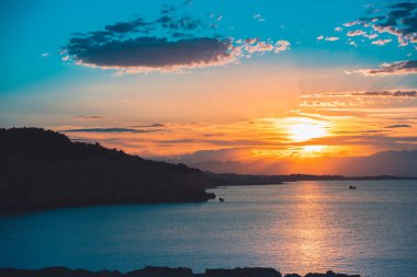 Dağların ve derin mavi okyanusun üzerinde inanılmaz renkli gökyüzü gün doğumu. Gün batımında deniz manzarası.