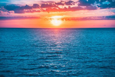 Denizde parlak, güzel bir gün doğumu. Sakin bir okyanusa yansıyan güneşin manzarası