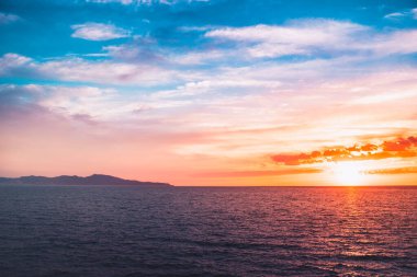 Dağların ve derin mavi okyanusun üzerinde inanılmaz renkli gökyüzü gün doğumu. Gün batımında deniz manzarası.