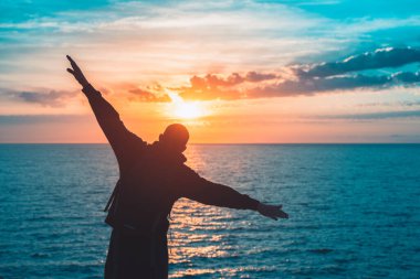 İnsan silueti uçurumun kenarında özgürlüğün tadını çıkarır ve güzel renkli gökyüzü ile denize bakar. Okyanusu yansıtan manzaralı bir güneş..
