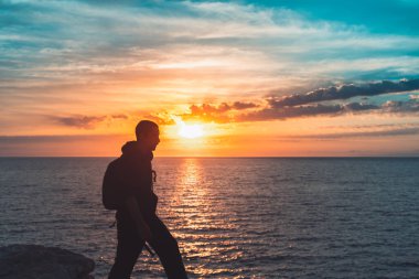 İnsan silueti uçurumun kenarında yürür ve güzel renkli gökyüzü ile denize bakar. Özgürlüğün tadını çıkarıyorum.