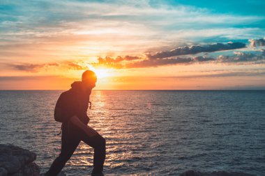 İnsan silueti uçurumun kenarında yürür ve güzel renkli gökyüzü ile denize bakar. Özgürlüğün tadını çıkarıyorum.