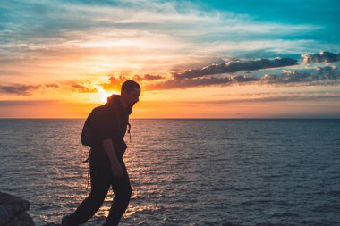 İnsan silueti uçurumun kenarında yürür ve güzel renkli gökyüzü ile denize bakar. Özgürlüğün tadını çıkarıyorum.
