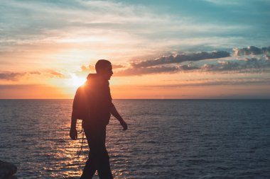 İnsan silueti uçurumun kenarında yürür ve güzel renkli gökyüzü ile denize bakar. Özgürlüğün tadını çıkarıyorum.