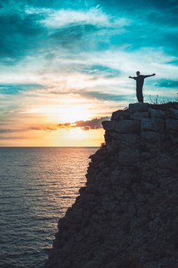 İnsan silueti uçurumun kenarında duruyor. Güzel renkli gökyüzü ile denize bakıyor..