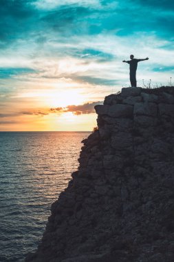 İnsan silueti uçurumun kenarında duruyor. Güzel renkli gökyüzü ile denize bakıyor..