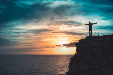 İnsan silueti uçurumun kenarında duruyor. Güzel renkli gökyüzü ile denize bakıyor..