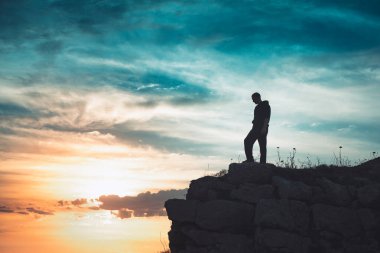 İnsan silueti uçurumun kenarında duruyor. Güzel renkli gökyüzü ile denize bakıyor..
