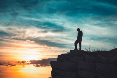 İnsan silueti uçurumun kenarında duruyor. Güzel renkli gökyüzü ile denize bakıyor..