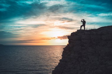 İnsan silueti uçurumun kenarında duruyor. Güzel renkli gökyüzü ile denize bakıyor..