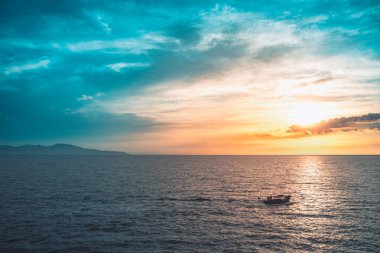 Dağların üstünde gün doğumu ve balıkçı teknesiyle derin mavi okyanus.