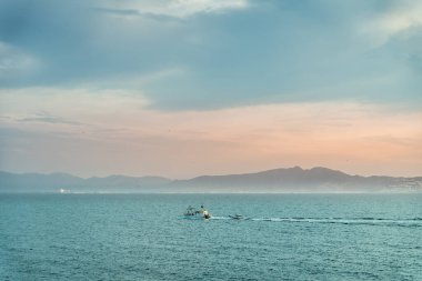 Dağların üstünde gün doğumu ve balıkçı teknesiyle derin mavi okyanus.