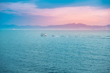 Dağların üstünde gün doğumu ve balıkçı teknesiyle derin mavi okyanus.