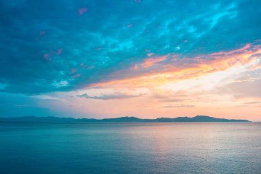 Sahil kayalıklarının ve denizin üzerinde turuncu renk yansımasıyla gün doğumu. Gün batımı ve renkli gökyüzü ile ufka karşı körfezin çarpıcı panoramik görüntüsü