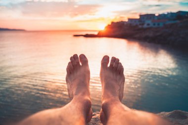 Çıplak ayaklı genç bir adamın bakış açısı deniz sahilinde gün batımında inanılmaz görünür. Akdeniz yaz tatillerinde dinlenir.