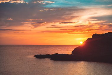 Sahil kayalıklarının ve denizin üzerinde turuncu renk yansımasıyla gün doğumu. Gün batımı ve renkli gökyüzü ile ufka karşı körfezin çarpıcı panoramik görüntüsü
