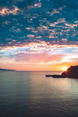 Sahil kayalıklarının ve denizin üzerinde turuncu renk yansımasıyla gün doğumu. Gün batımı ve renkli gökyüzü ile ufka karşı körfezin çarpıcı panoramik görüntüsü