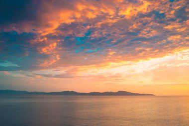 Sahil kayalıklarının ve denizin üzerinde turuncu renk yansımasıyla gün doğumu. Gün batımı ve renkli gökyüzü ile ufka karşı körfezin çarpıcı panoramik görüntüsü