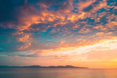 Sahil kayalıklarının ve denizin üzerinde turuncu renk yansımasıyla gün doğumu. Gün batımı ve renkli gökyüzü ile ufka karşı körfezin çarpıcı panoramik görüntüsü