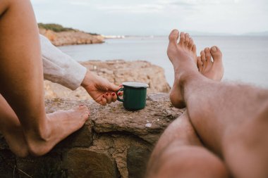 Çıplak ayakla denize bakan ve içecek içen bir çift. Sabah tatili. Akdeniz kıyıları. Yaz turistlerini rahatlatmak..