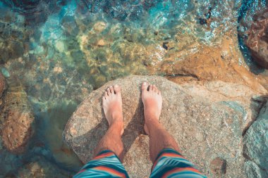 Çıplak ayaklı genç adamın bakış açısı deniz sahilindeki turkuaz suda duruyor. Akdeniz yaz tatillerinde dinlenir.