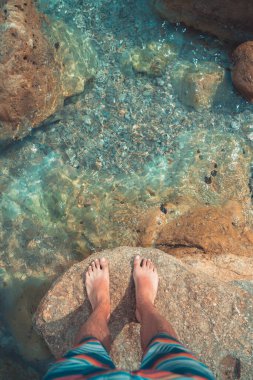 Çıplak ayaklı genç adamın bakış açısı deniz sahilindeki turkuaz suda duruyor. Akdeniz yaz tatillerinde dinlenir.