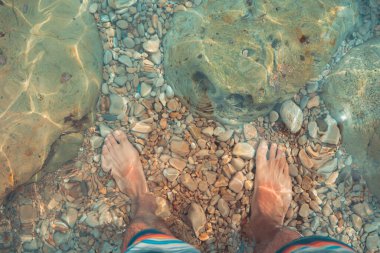 Çıplak ayaklı genç adamın bakış açısı deniz sahilindeki turkuaz suda duruyor. Akdeniz yaz tatillerinde dinlenir.