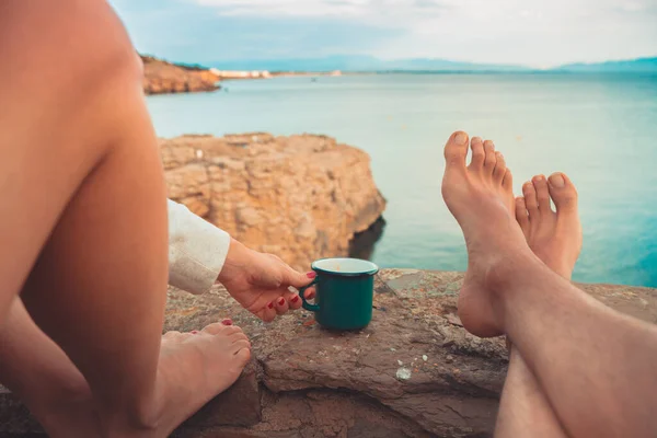 Couple with bare foot look at sea while drinks a beverage. Morning holiday routine Mediterranean coast relax summer tourist.