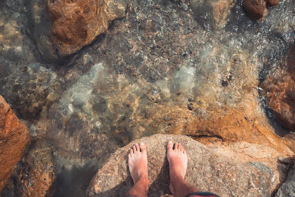 Çıplak ayaklı genç adamın bakış açısı deniz sahilindeki turkuaz suda duruyor. Akdeniz yaz tatillerinde dinlenir.