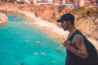 Akdeniz kıyı şeridi manzaralı destansı ve ilham verici genç gezgin dağ kayalıklarından türkuaz suya bakıyor. Katalonya sahilinde yaz tatili. İspanya kıyı şeridinde sırt çantaları.