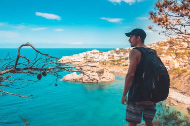 Akdeniz kıyı şeridi manzaralı destansı ve ilham verici genç gezgin dağ kayalıklarından türkuaz suya bakıyor. Katalonya sahilinde yaz tatili. İspanya kıyı şeridinde sırt çantaları.