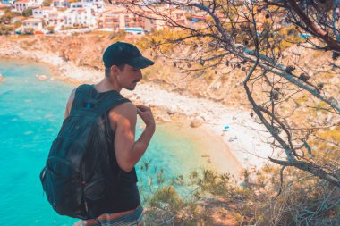 Akdeniz kıyı şeridi manzaralı destansı ve ilham verici genç gezgin dağ kayalıklarından türkuaz suya bakıyor. Katalonya sahilinde yaz tatili. İspanya kıyı şeridinde sırt çantaları.