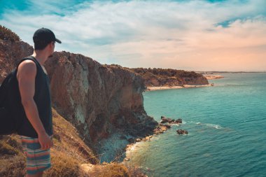 Akdeniz kıyı şeridi manzaralı destansı ve ilham verici genç gezgin dağ kayalıklarından türkuaz suya bakıyor. Katalonya sahilinde yaz tatili. İspanya kıyı şeridinde sırt çantaları.