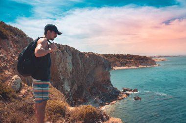 Akdeniz kıyı şeridi manzaralı destansı ve ilham verici genç gezgin dağ kayalıklarından türkuaz suya bakıyor. Katalonya sahilinde yaz tatili. İspanya kıyı şeridinde sırt çantaları.