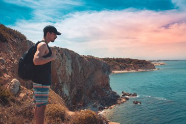 Akdeniz kıyı şeridi manzaralı destansı ve ilham verici genç gezgin dağ kayalıklarından türkuaz suya bakıyor. Katalonya sahilinde yaz tatili. İspanya kıyı şeridinde sırt çantaları.