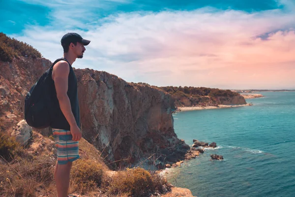 Epic and inspiring young traveller at mediterranean coastline view looking at turquoise water from mountain cliffs. Summer holiday in Catalonia beach. Backpacking in Spain coastline.